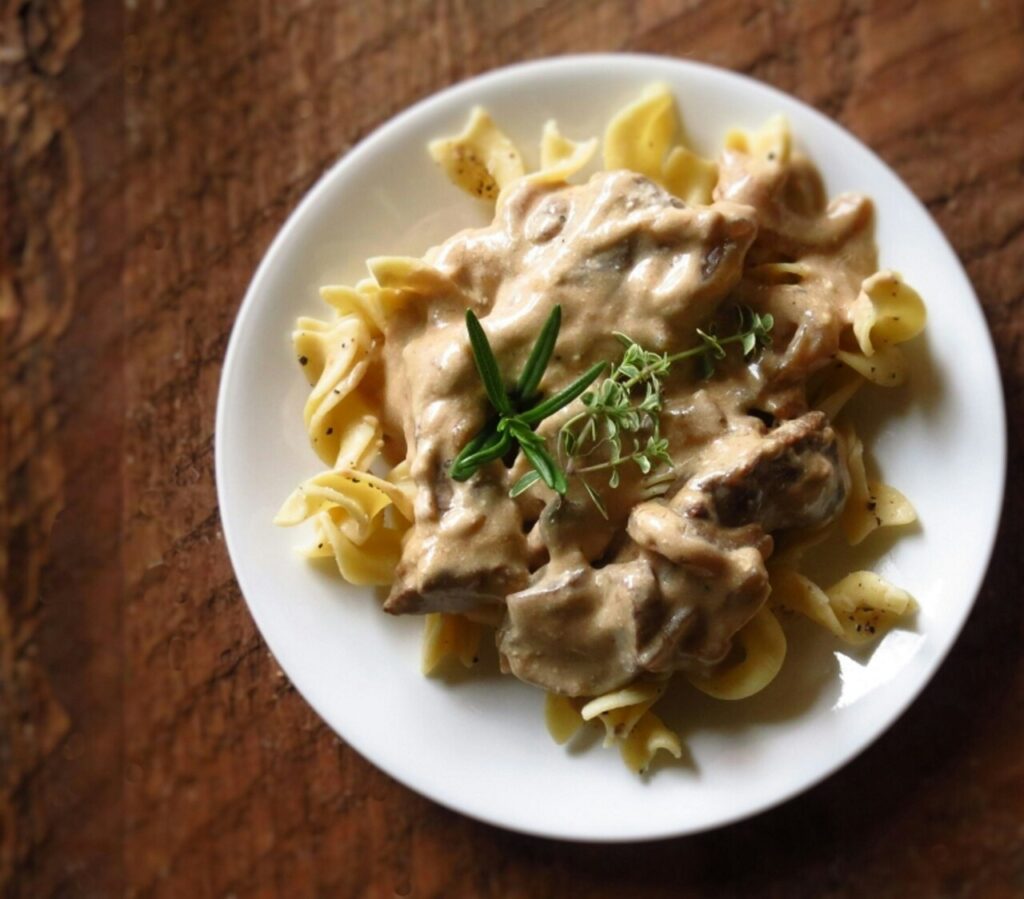 Beef stroganoff served over egg noodles, garnished with fresh herbs