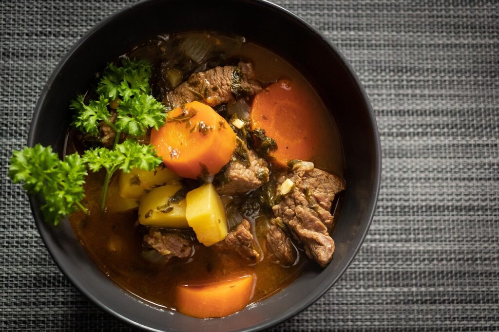 Close-up of a steaming bowl of beef stew with carrots, potatoes, and fresh parsley.