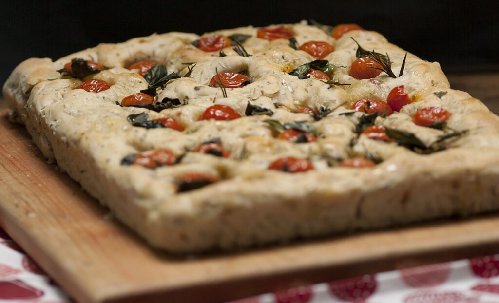 A tray of golden focaccia topped with rosemary sprigs and flaky salt.