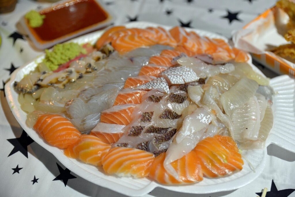 A hand dipping sashimi into soy sauce with wasabi on the side.