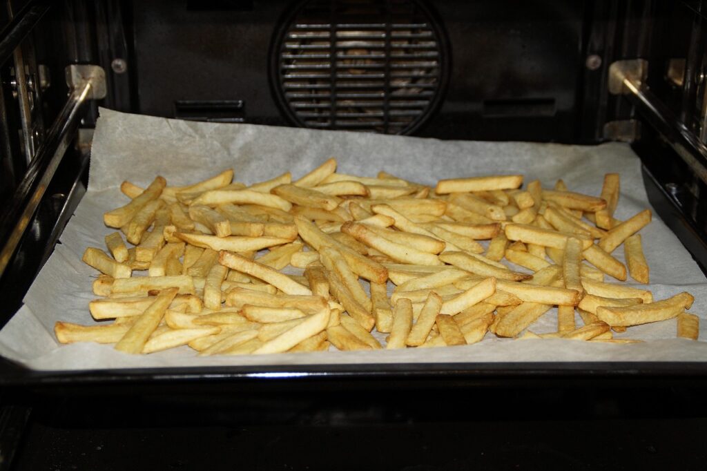 Hot baking sheet preheated in the oven with fries arranged on it.