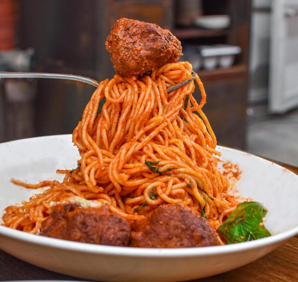 Pasta twirled on a fork over a plate of sauce-covered meatballs.