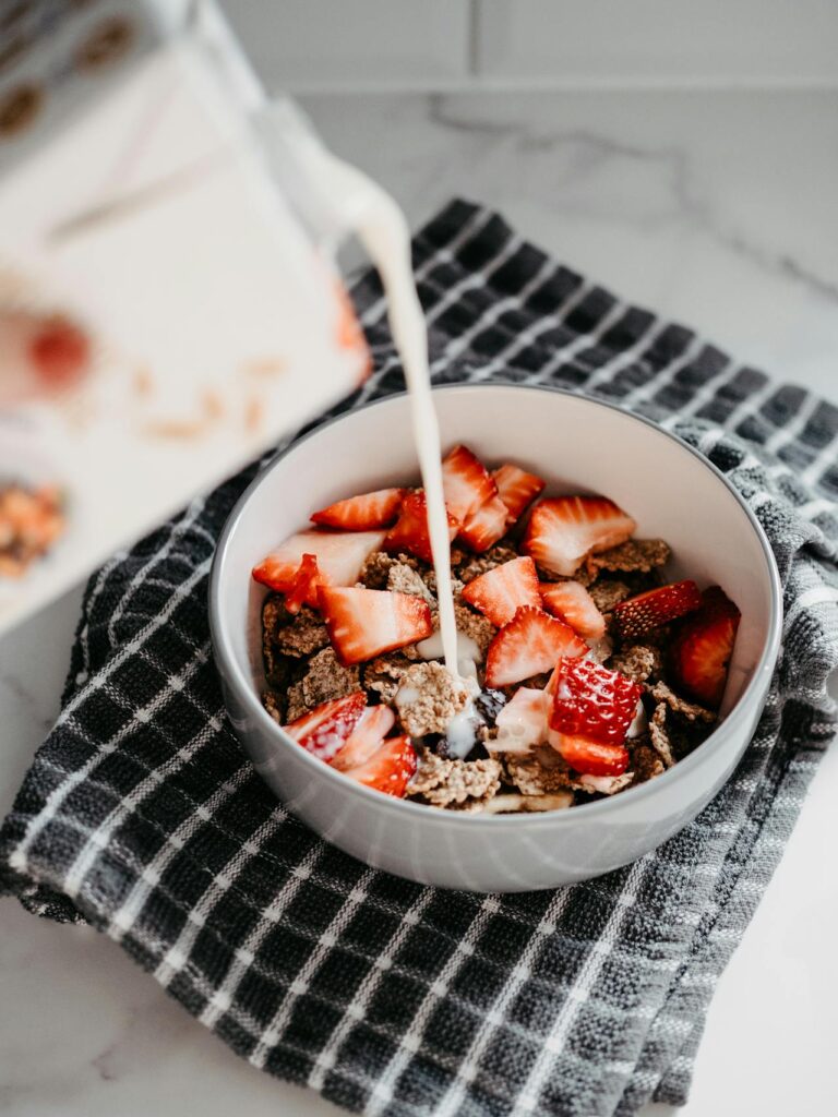 A bowl of corn flakes with milk and fresh strawberries.