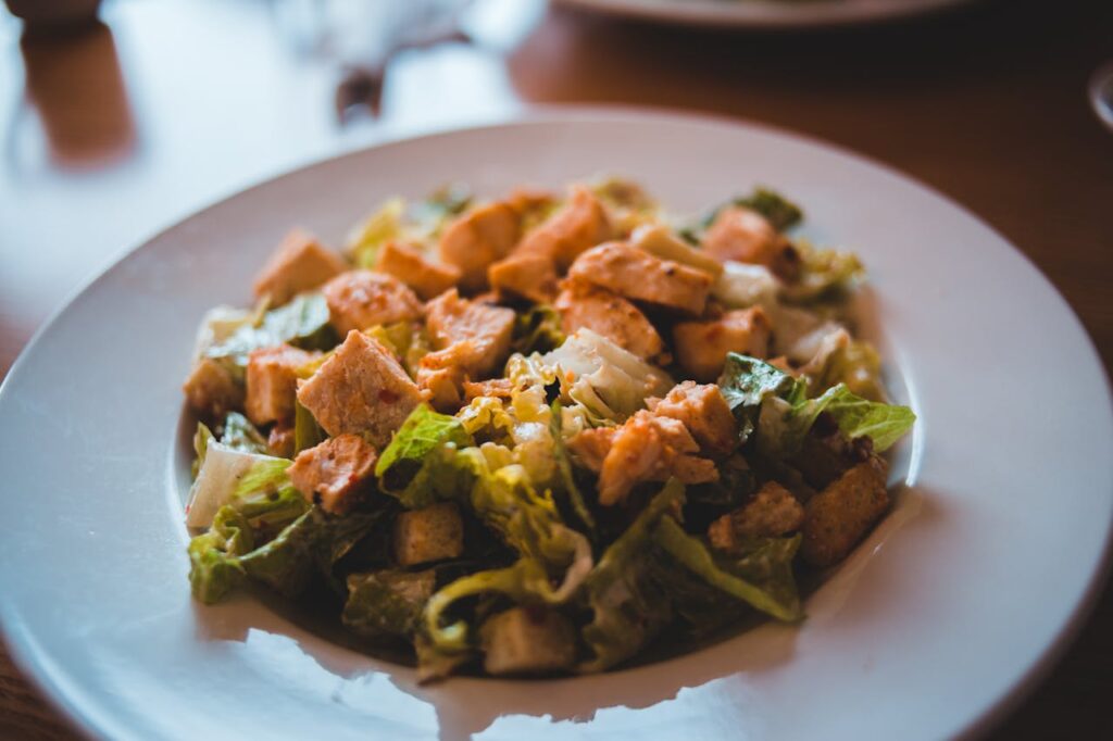 Plated chicken chunks in salad with fresh vegetables.