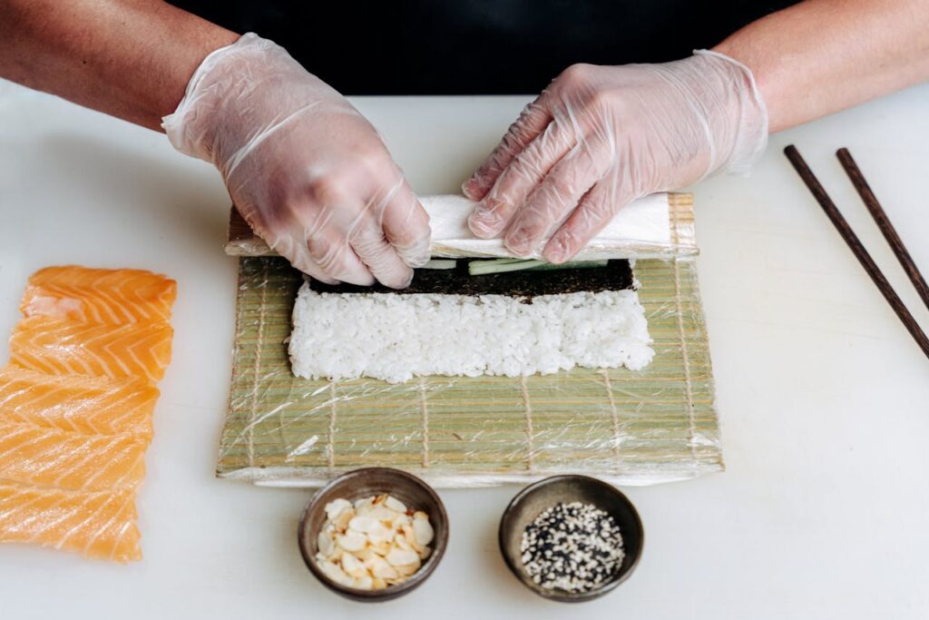 A sushi chef carefully slicing fish for sashimi next to sushi being rolled on a bamboo mat.