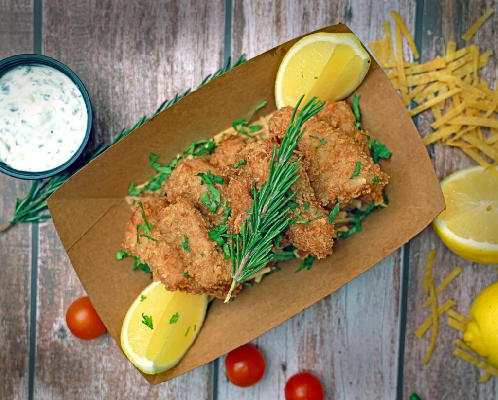 A tray with fried fish, lemon wedges and tomatoes