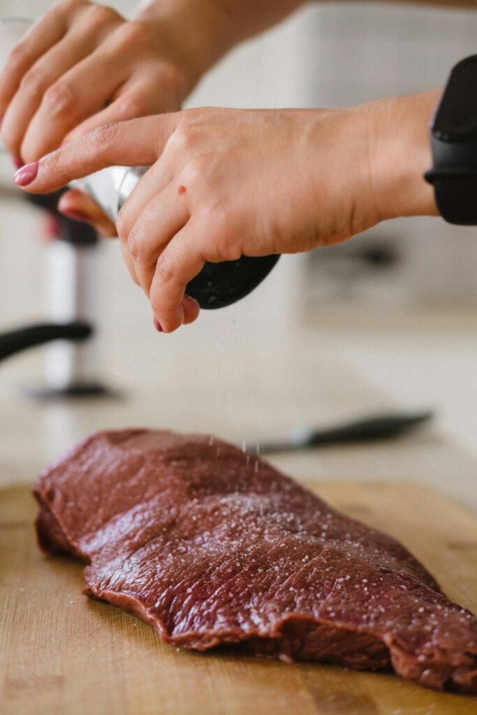 Hands Salting Piece of Raw Meat