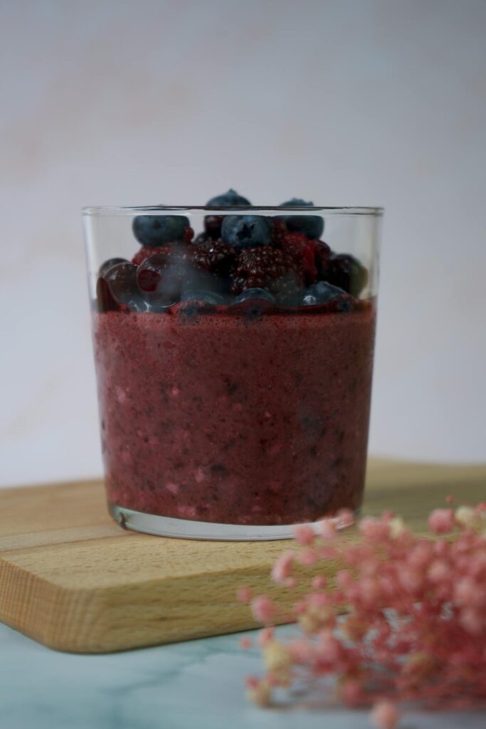 A tall glass of berry smoothie with fresh fruit on the side.