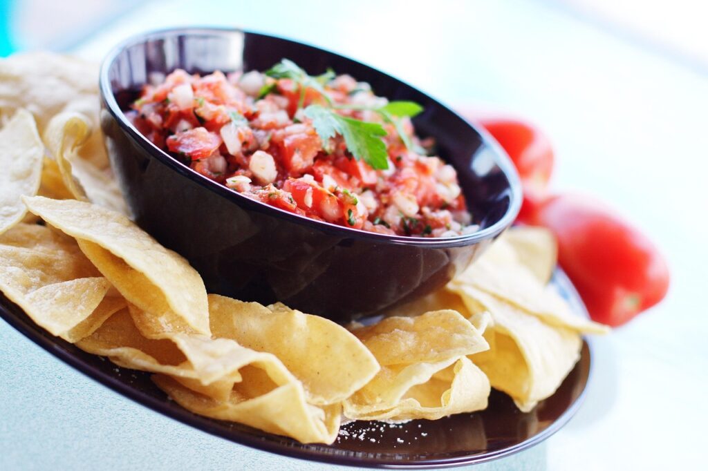 A bowl of colorful salsa fresca with tortilla chips arranged around it.