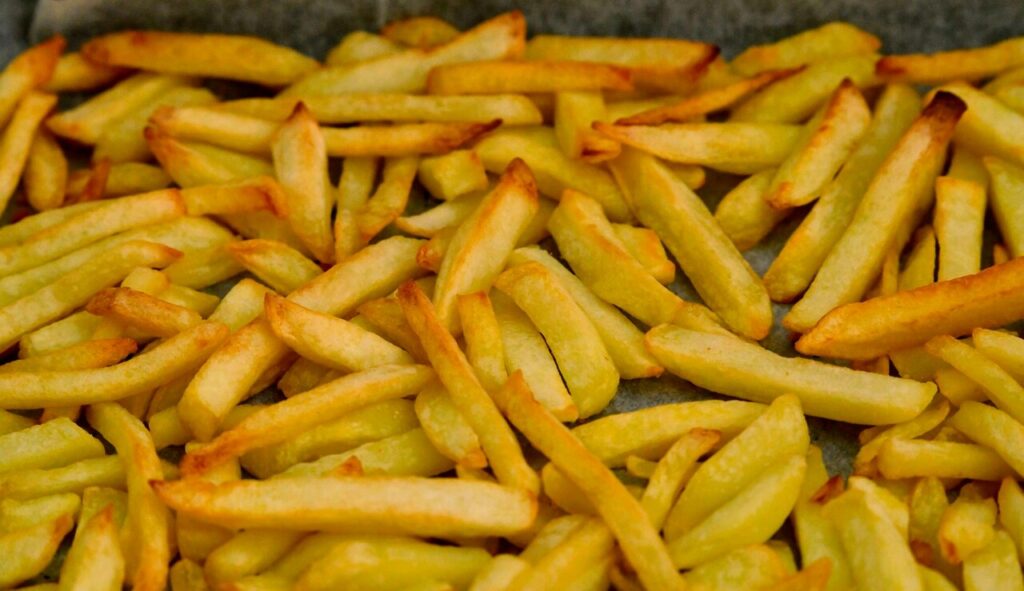 Fries spread in a single layer on a parchment-lined baking tray.