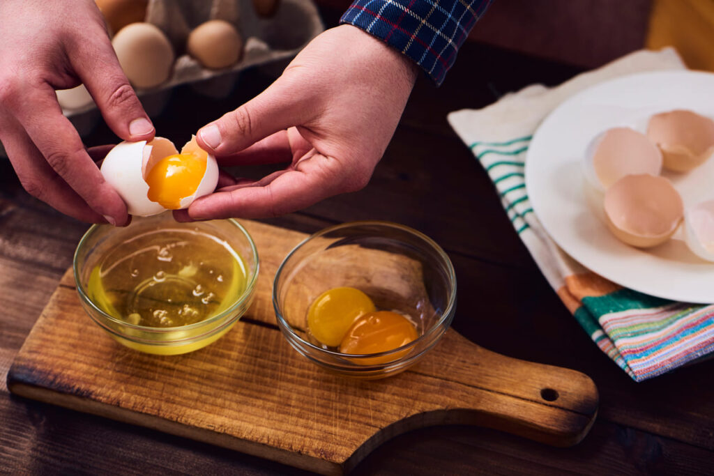 Brown and white eggs cracked into bowls showing similar yolks.