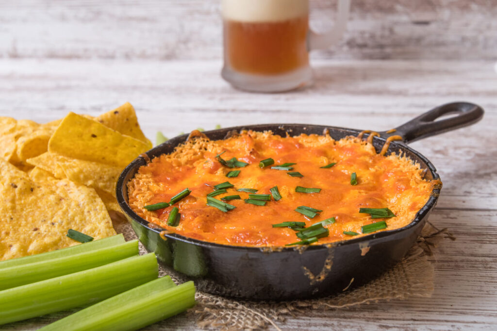 A bubbling casserole dish of buffalo chicken dip with chips and celery on the side.