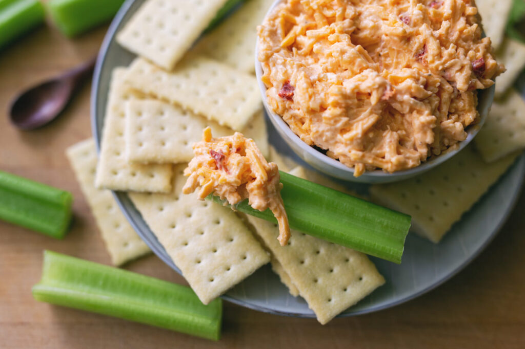 A small serving dish of pimento cheese dip with crackers and celery sticks on the side.