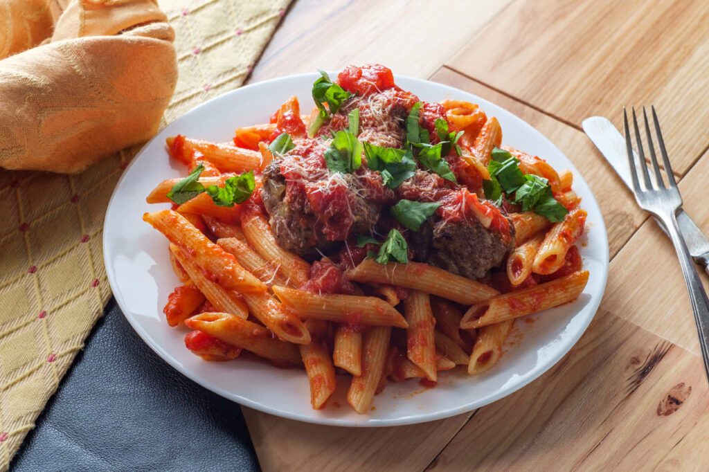 Italian penne rigate pasta with sugo all'arrabbiata sauce and meatballs garnished with chopped basil and parmesan cheese