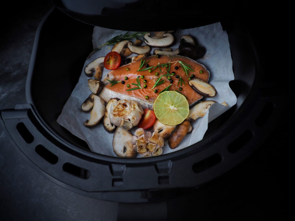 Fresh Salmon fillet with thyme, garlic and lemon slices,shiitake mushroom  tomatoes in air-fryer.clean and healthy food in dark tone.