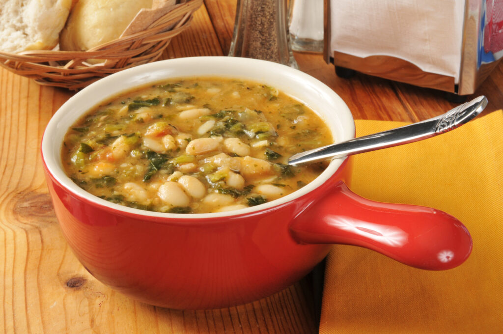 A bowl of healthy kale and white bean soup with dinner rolls