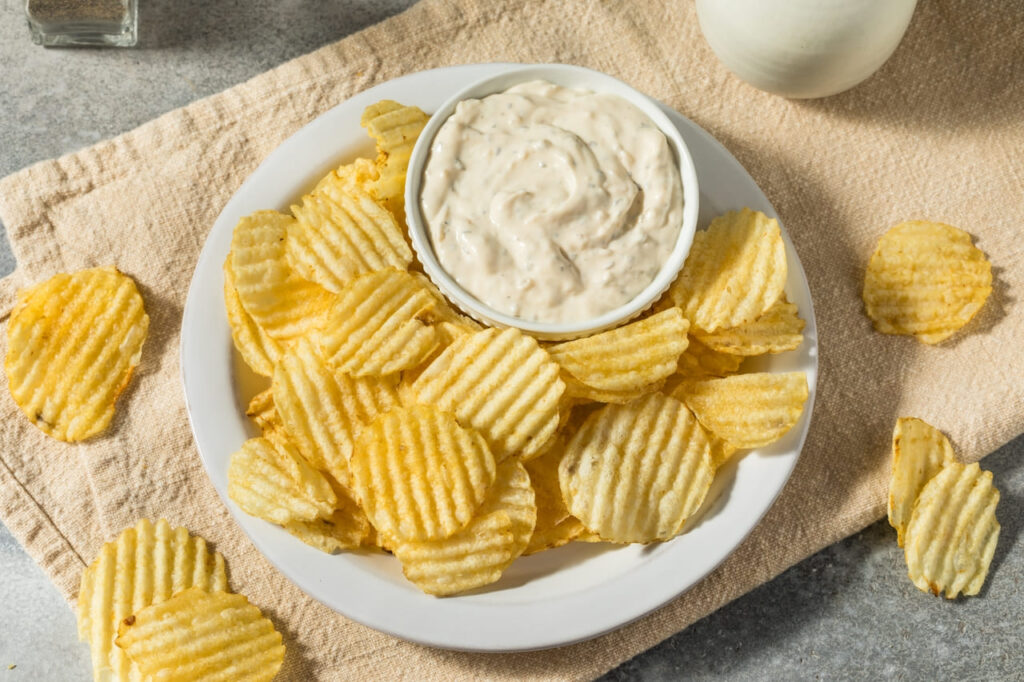 A small bowl of French onion dip with ridged potato chips scattered nearby.