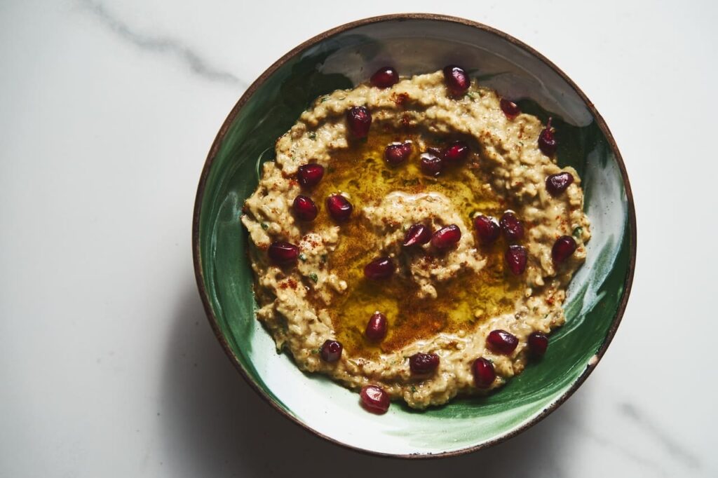 A rustic bowl of baba ganoush drizzled with olive oil and sprinkled with parsley, served with pita bread.