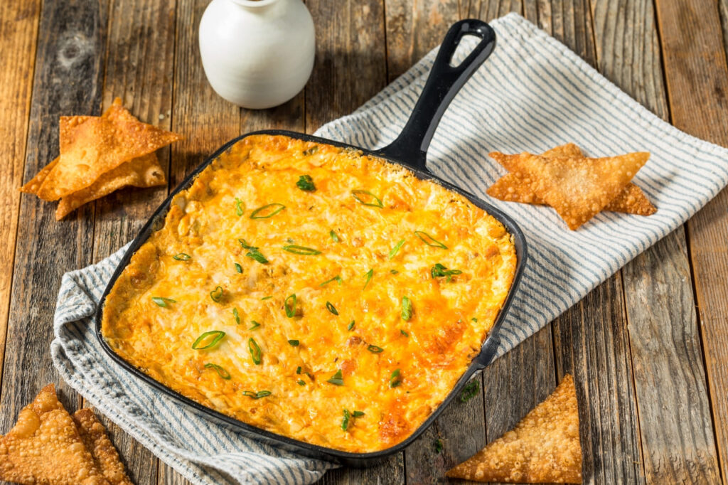 A baking dish of crab rangoon dip with golden wonton chips beside it.