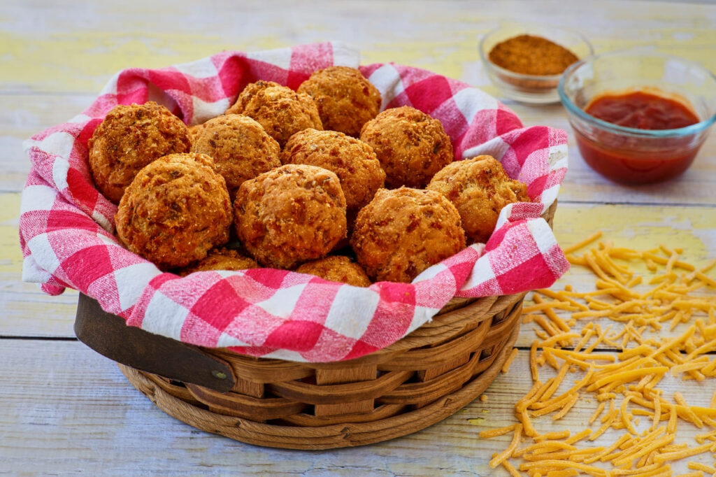 Basket of golden hushpuppies with a side of dipping sauce.