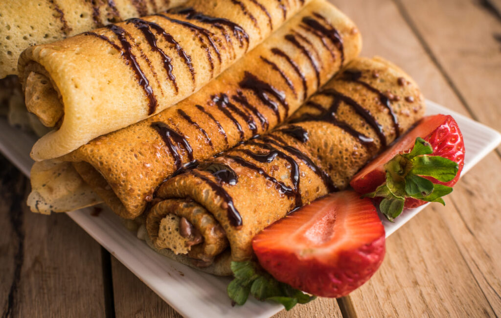 Crepes with nutella and strawberries. Rustic wooden background.