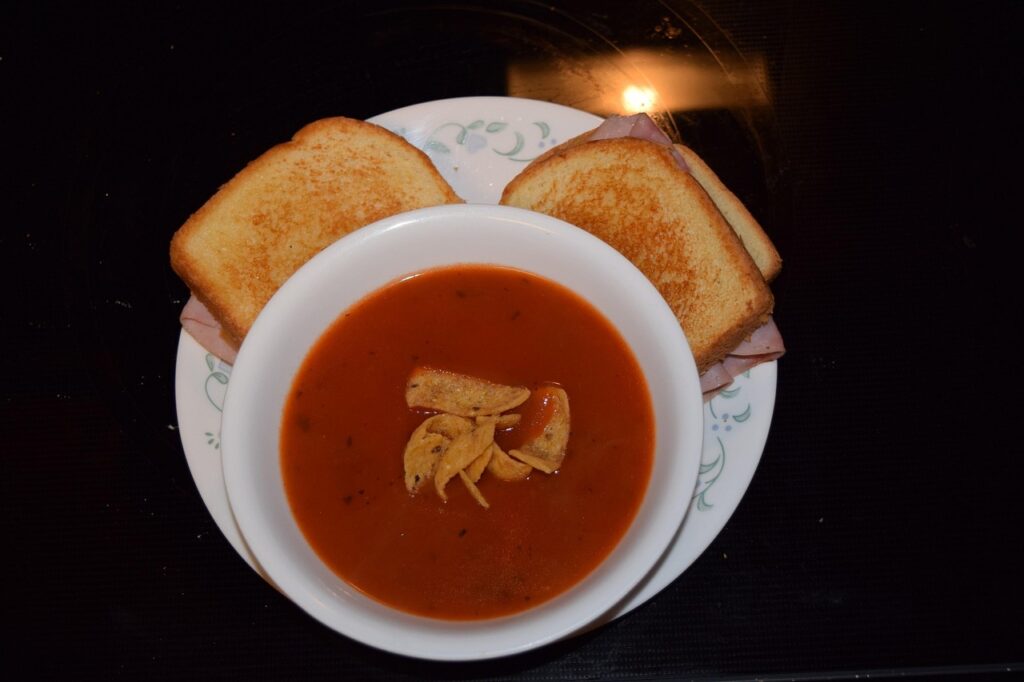 Sandwich halves stacked beside a steaming bowl of tomato soup.