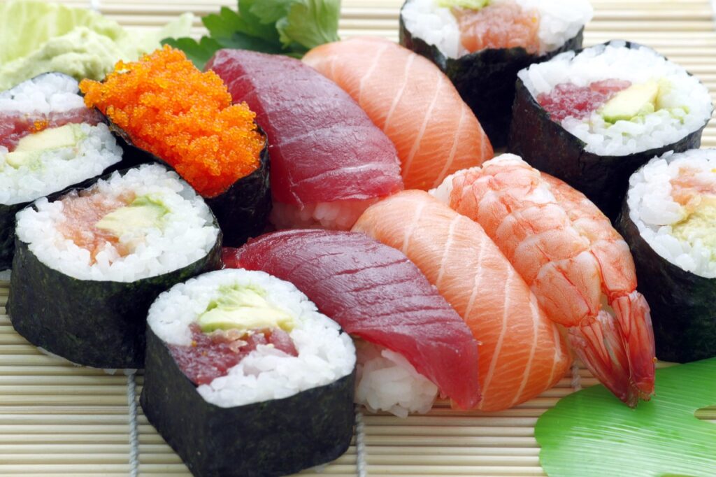 A nutrition-style flat lay showing salmon sashimi, sushi rolls, and fresh vegetables.