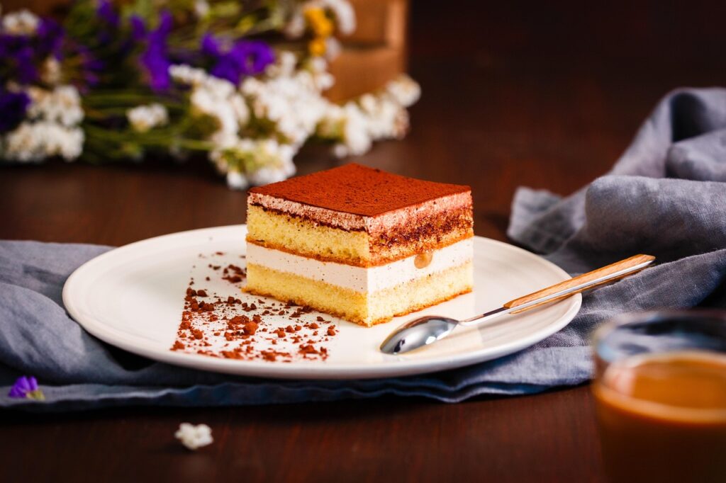 A square of tiramisu dusted with cocoa powder, served on a simple white plate with a fork.