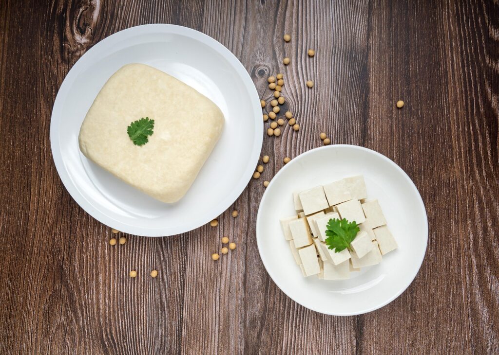 Fresh tofu cubes on a wooden board with soybeans scattered around.
