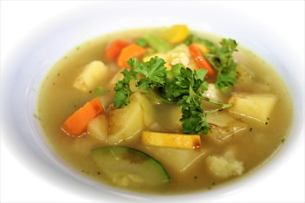 A pot of creamy vegetable soup with visible roasted carrots, potatoes, and herbs.