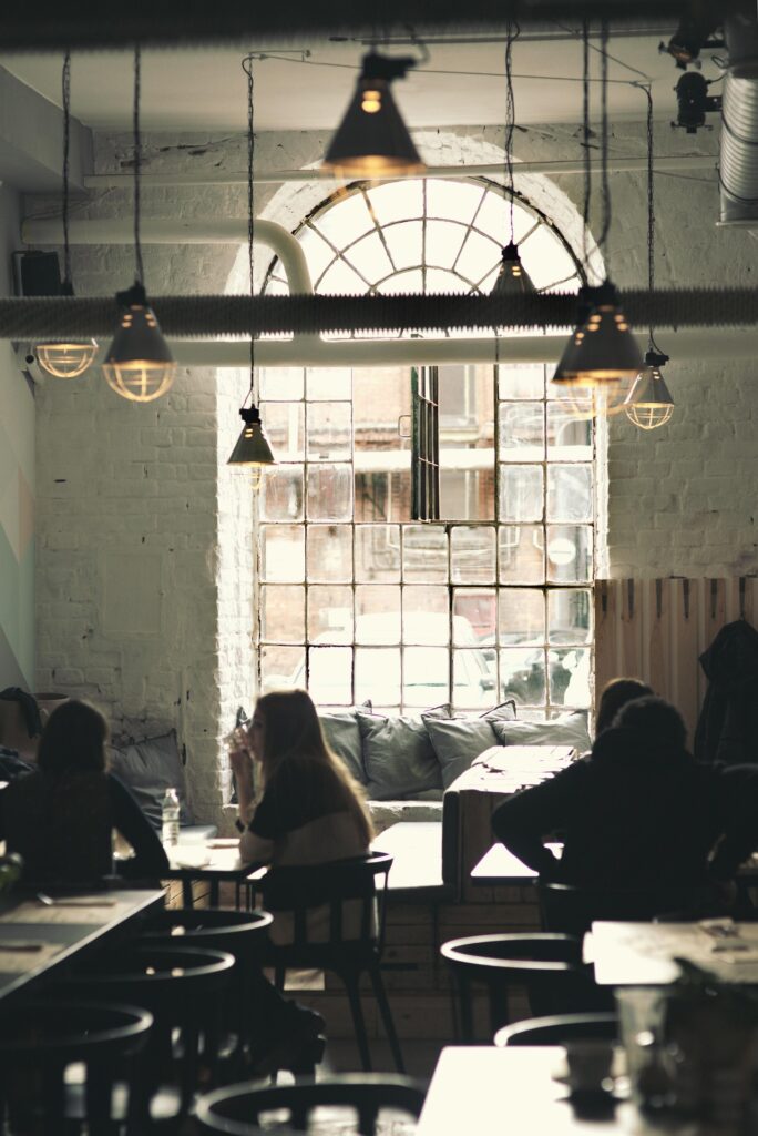 A cozy, vintage-style coffeehouse scene with people engaged in lively conversation, old books and newspapers on tables, and a sense of history in the décor.