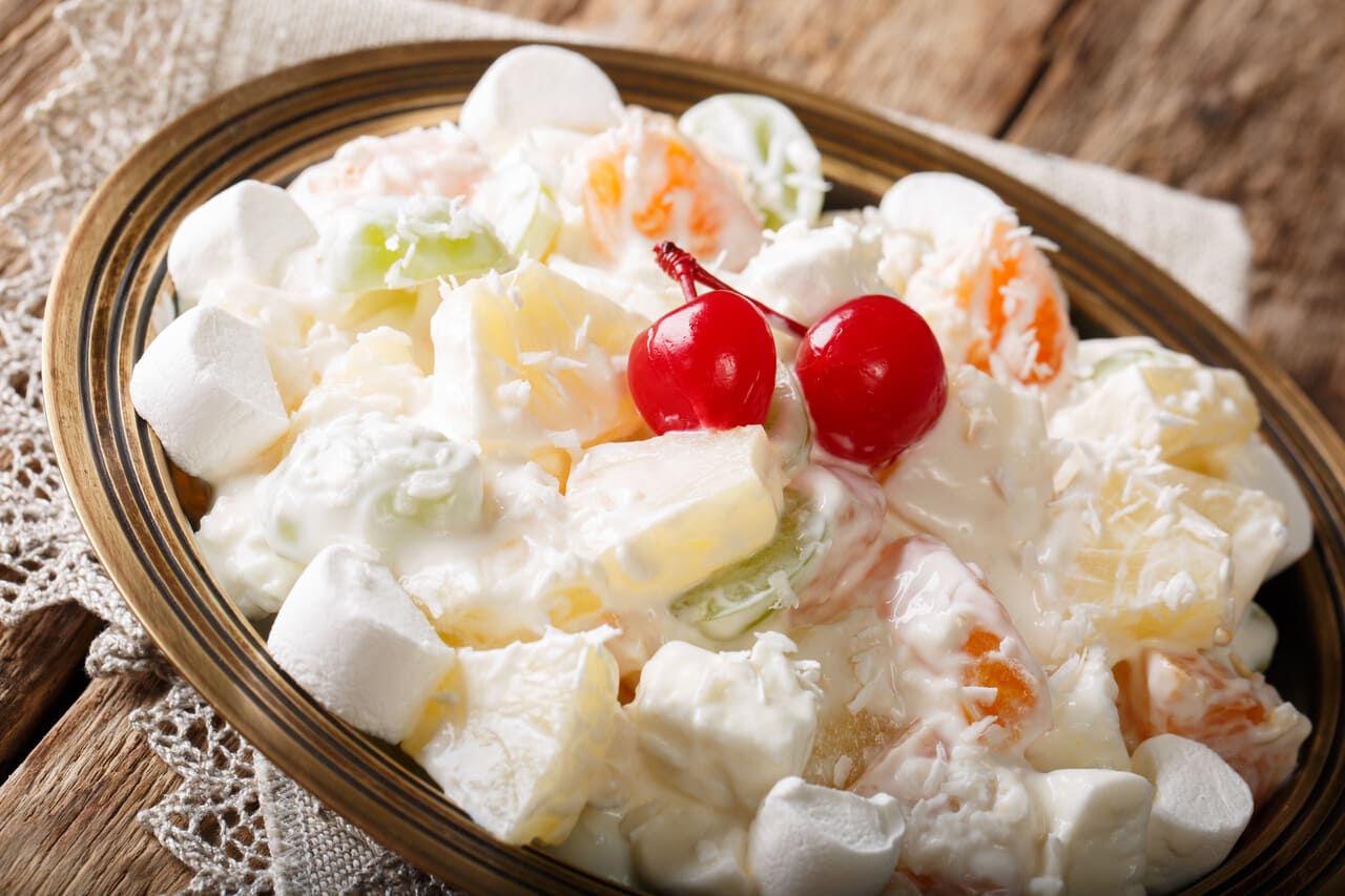 Light fruit salad Ambrosia with marshmallow and vanilla yogurt close-up on a plate.